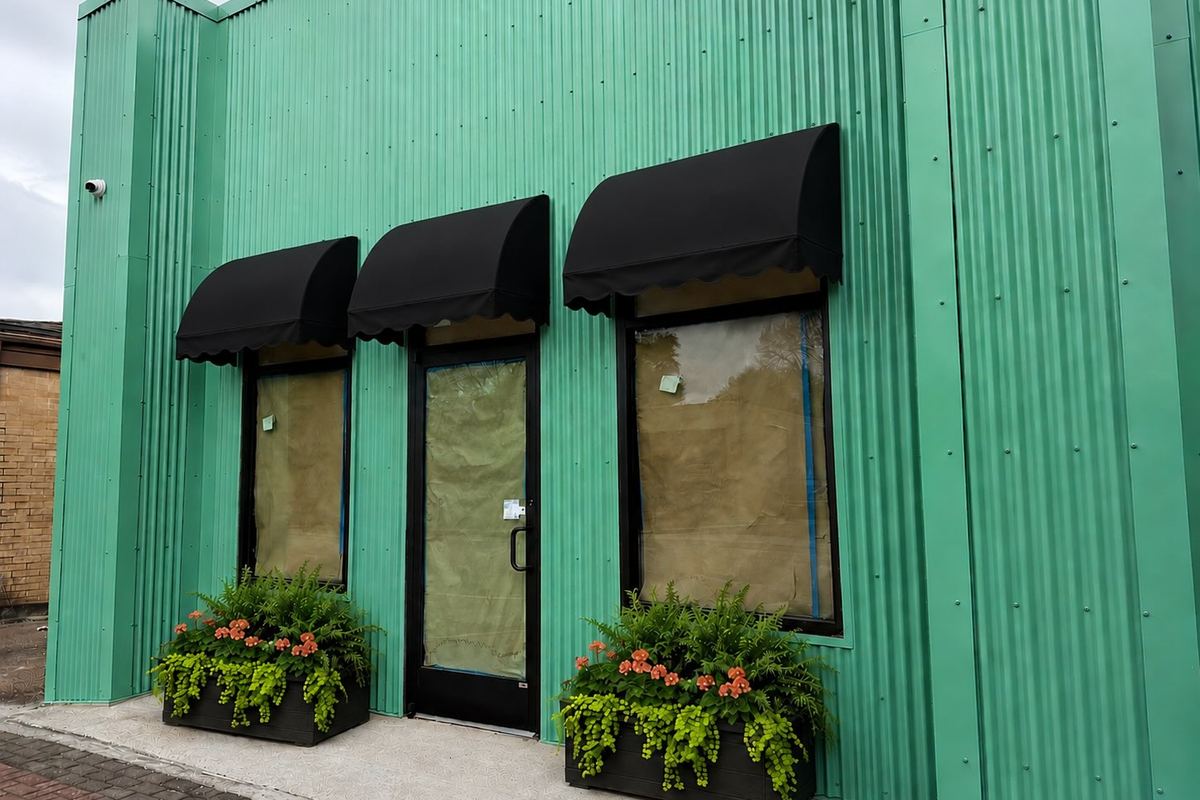 Mint-green building with black scalloped awnings and flower planters at Southern Vintage Collective on Calder Ave