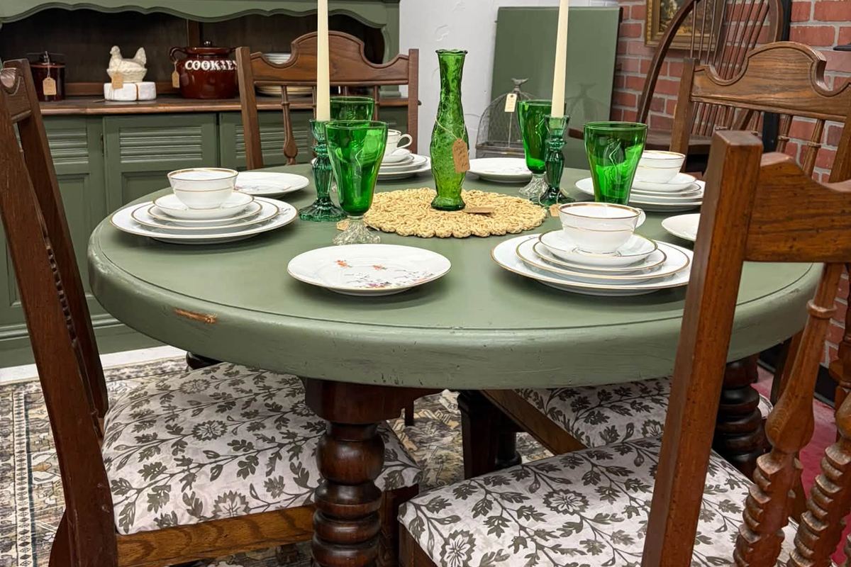 Green antique dining table set with green glassware in front of a painted hutch at The Squirrel's Nest
