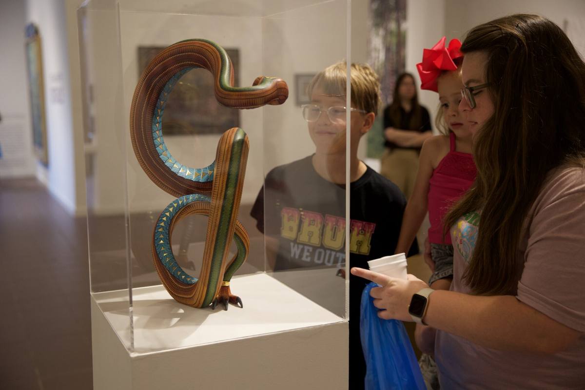 Visitors look at a coiled, striped serpent sculpture in a glass case inside a gallery at the Art Museum of Southeast Texas