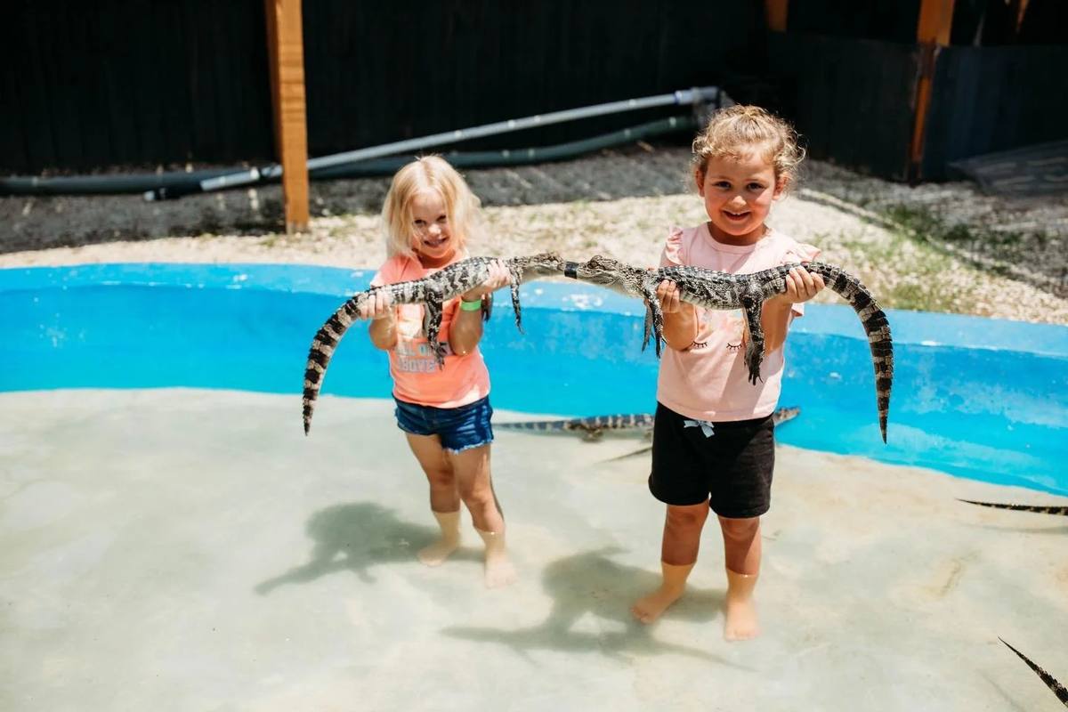 Two young girls stand in a shallow pool holding baby alligators at Gator Country in Beaumont