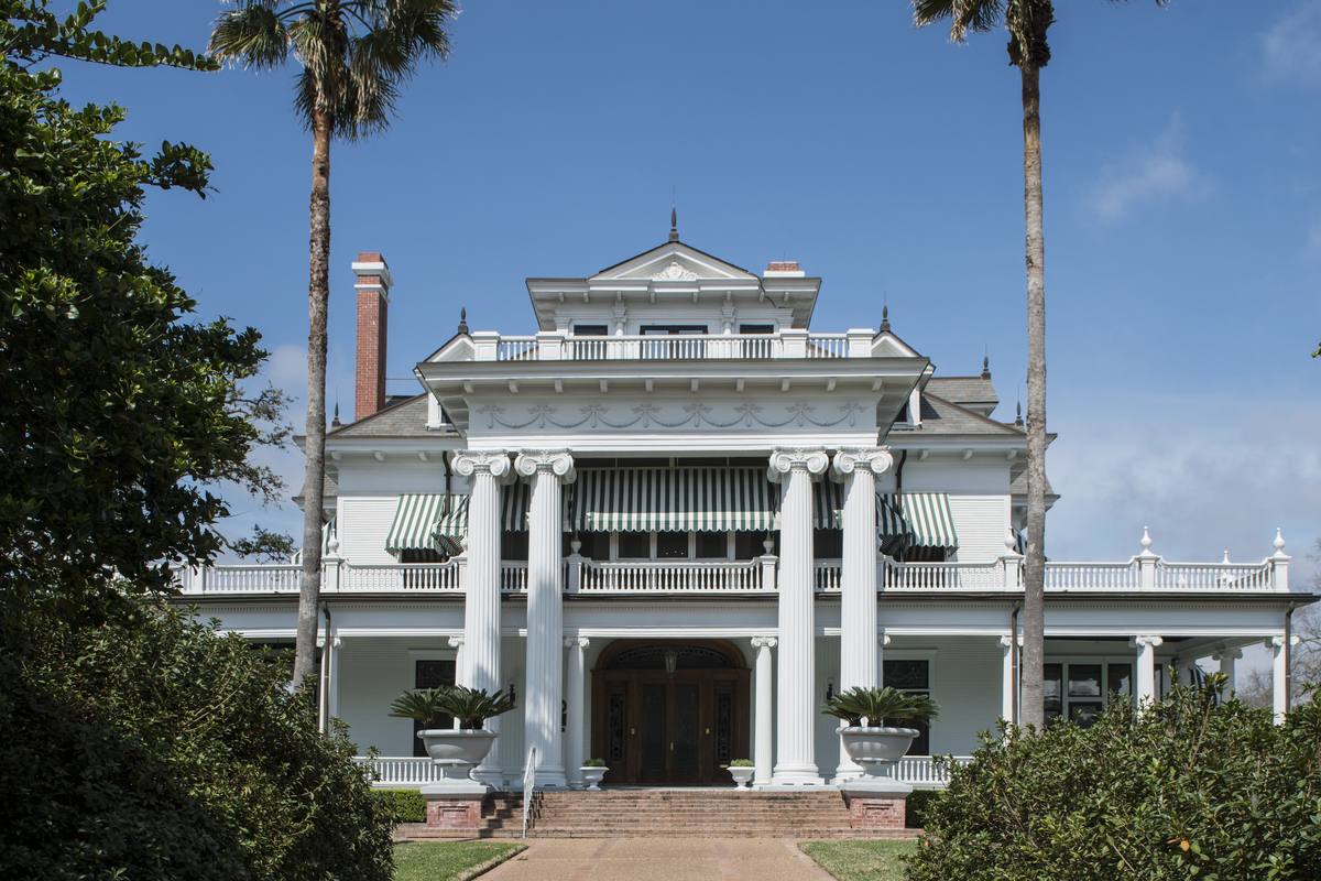The front of the McFaddin-Ward House in Beaumont, a white Beaux-Arts Colonial Revival mansion with tall Ionic columns and striped awnings