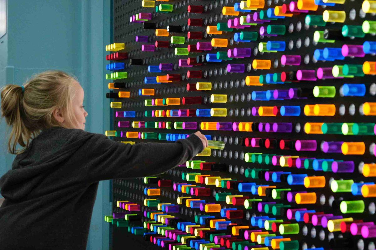 A young girl reaches out to place a glowing colored peg on a giant peg-light wall at the Beaumont Children's Museum
