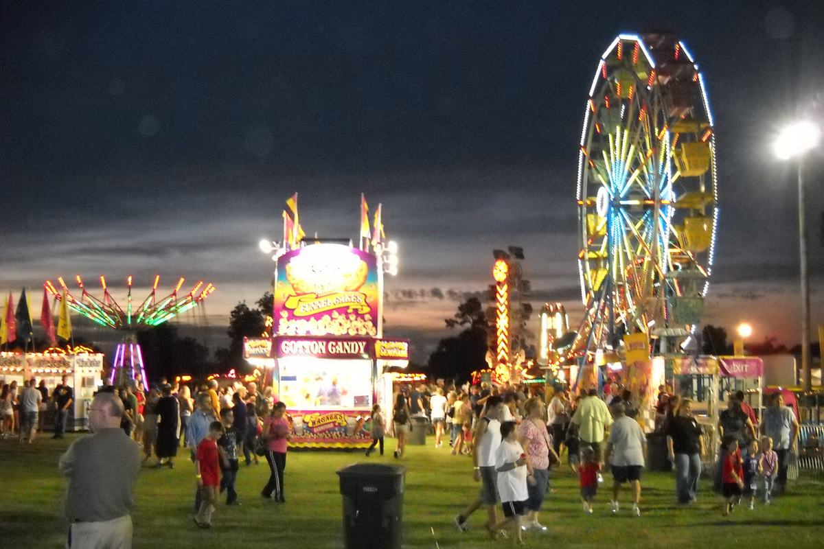 Crowds walk across the grass at night past a cotton candy stand, lit carnival rides and a Ferris wheel at the Groves Pecan Festival in 2010