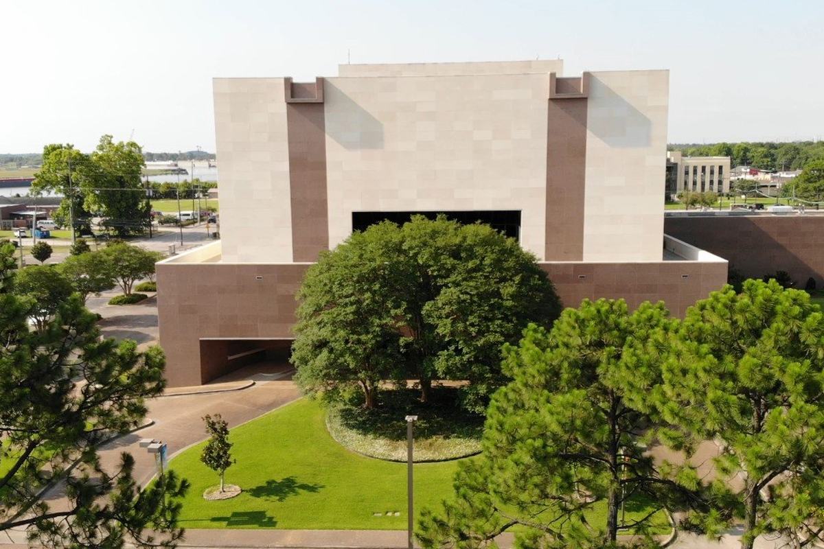 An aerial view of the Lutcher Theater in Orange, a tall pale stone building with a round lawn and a large shade tree at its entrance