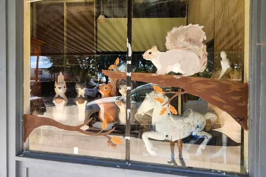 The Squirrel's Nest front window in Silsbee, painted with a white squirrel on an oak branch above an antique carousel horse